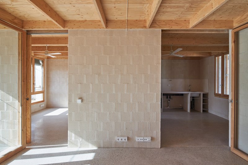 Open interior with exposed timber beams and ribbed hempcrete partition wall dividing the concrete floor space