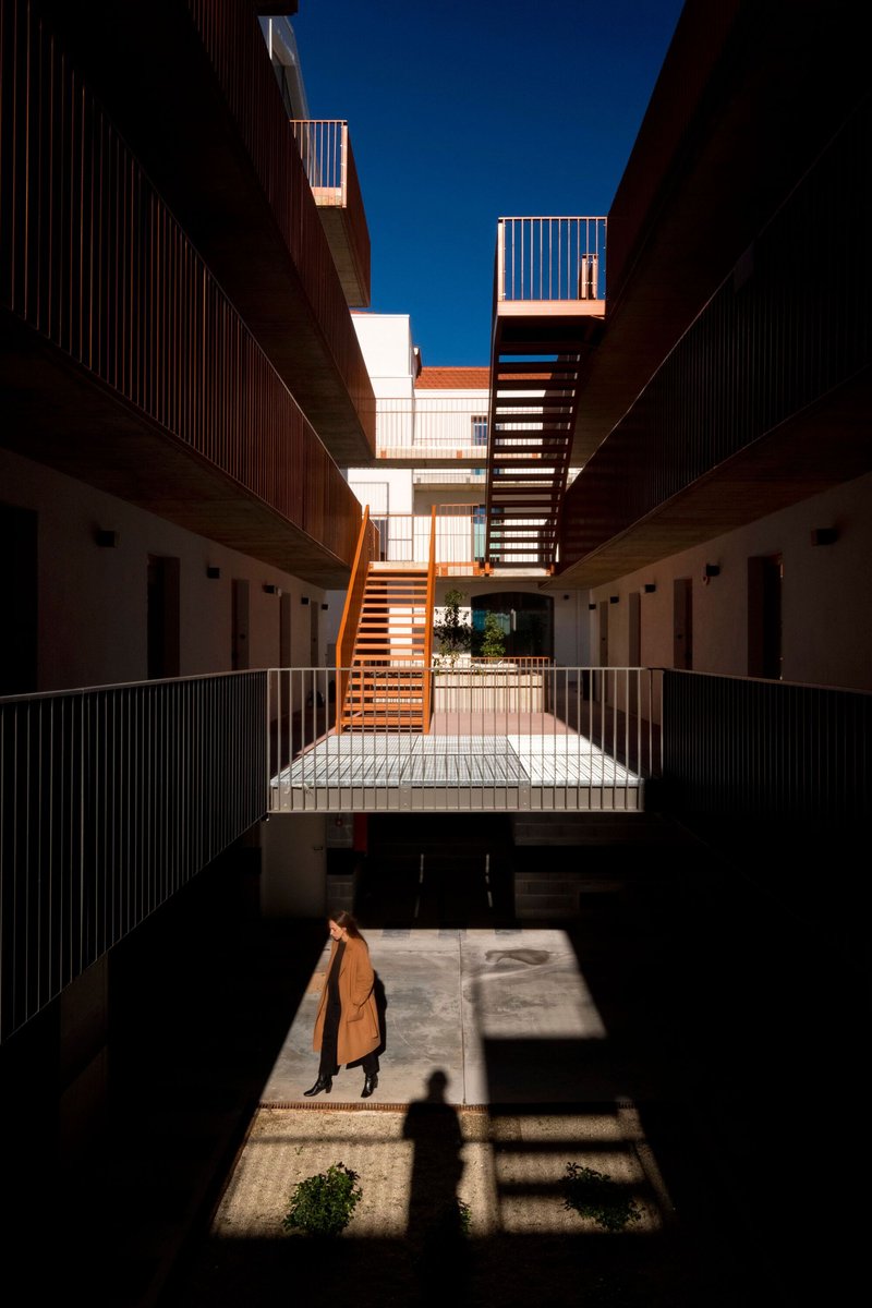 Interior courtyard with diagonal steel staircase connecting tiered access galleries in bright sun