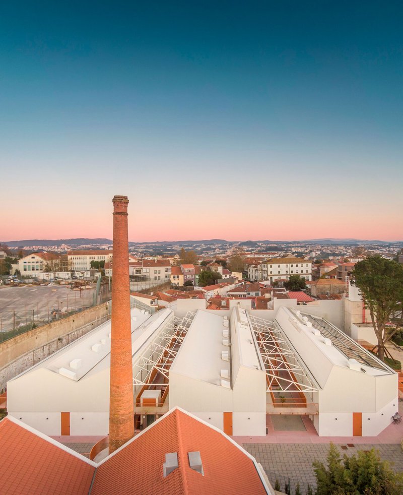 Elevated view showing white sawtooth roofs with exposed steel trusses and a brick chimney at sunset