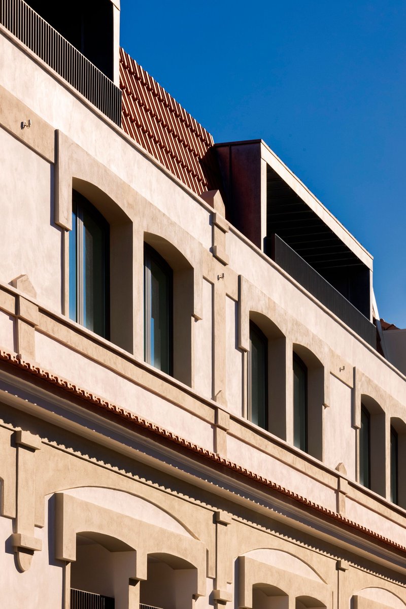 Layered facade with arched openings in rendered masonry topped by corrugated metal screening