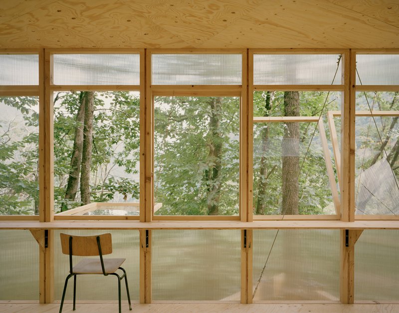 Interior wall with timber framing, translucent lower panels and clear upper glazing facing the forest