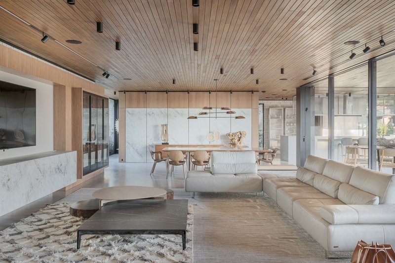 Open living and dining area with slatted timber ceiling and pendant lights above light wood flooring