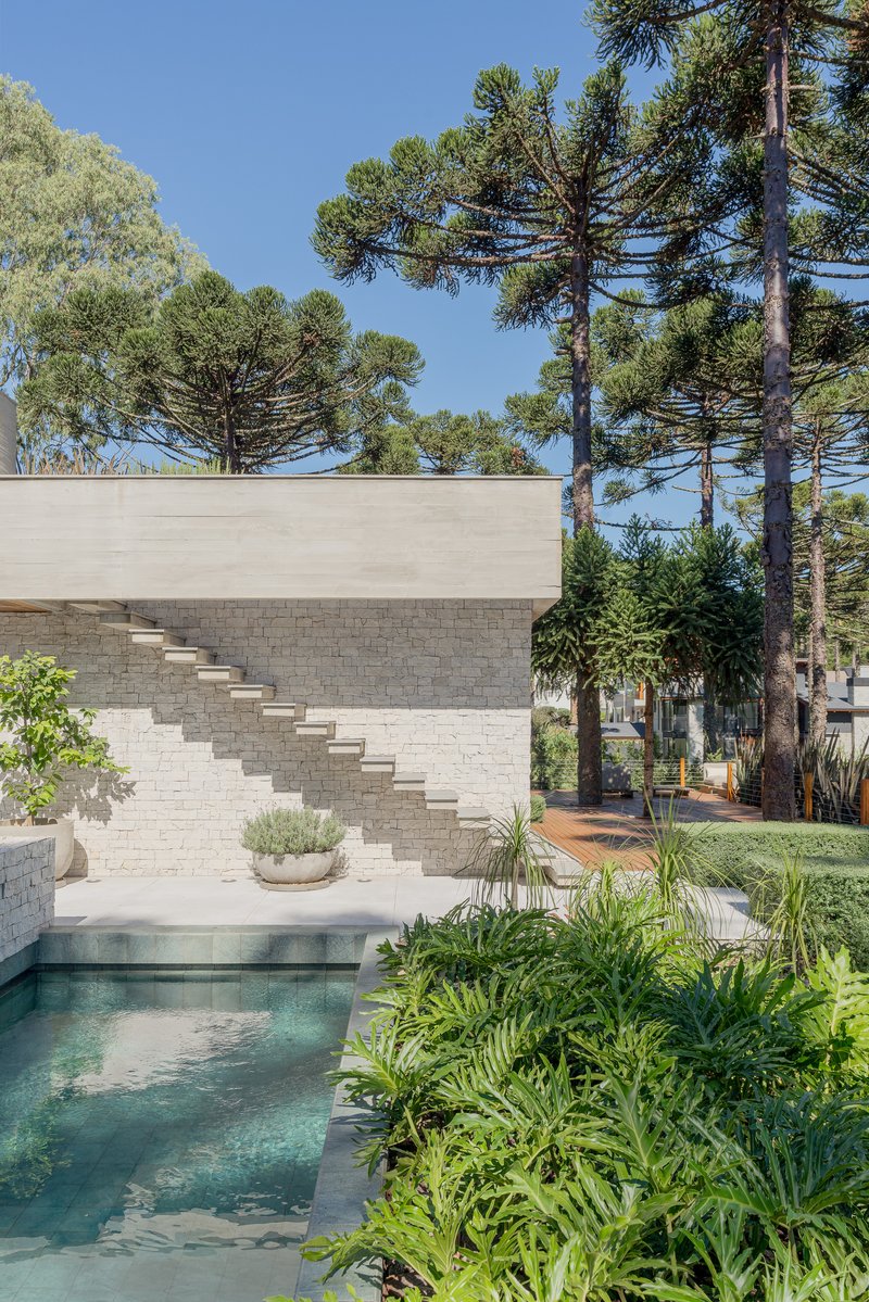 External staircase on white masonry wall beside pool with tropical planting and pine canopy
