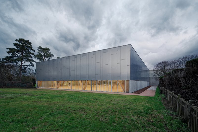 Side elevation showing metal cladding above timber-framed glazed base at twilight