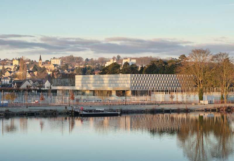 Waterfront view of the low horizontal building with patterned facade reflected in the calm river at dusk