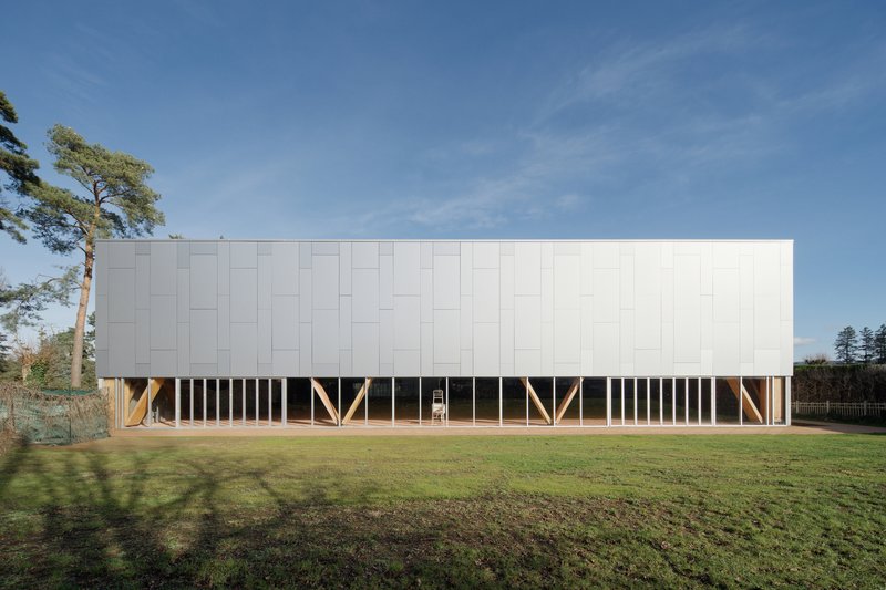 White paneled volume elevated on timber diagonal supports above lawn under a clear blue sky