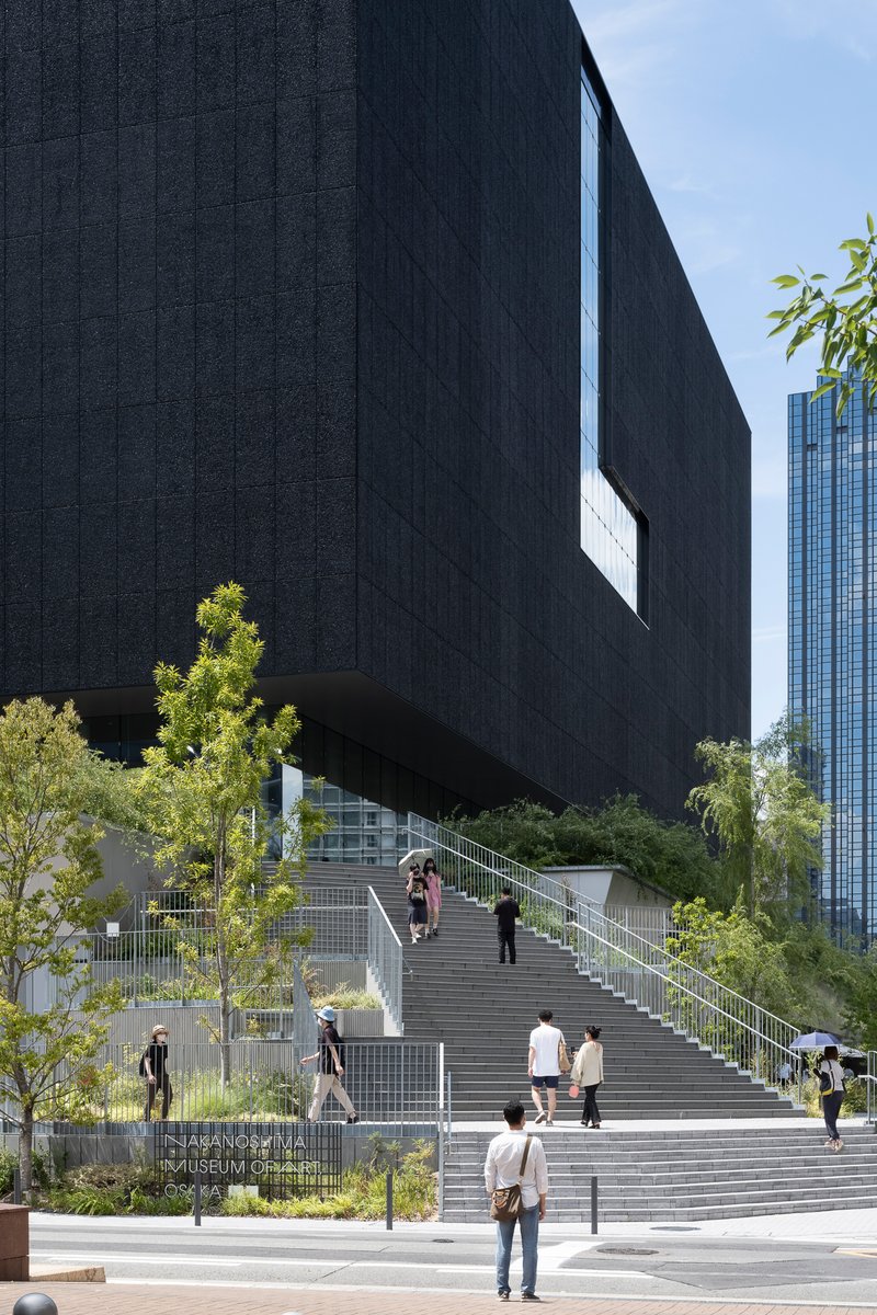 Wide staircase with visitors ascending beneath the cantilevered dark mass and surrounding greenery