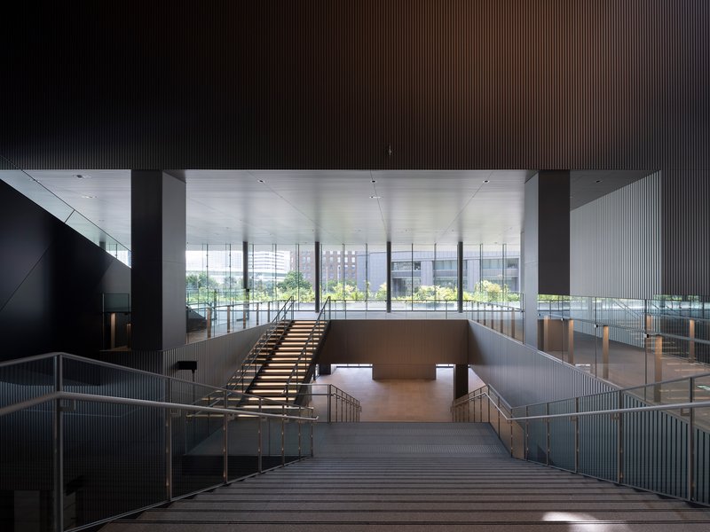 Central timber staircase descending toward perimeter glazing with park greenery visible beyond