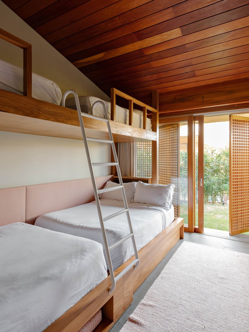 Bunk bedroom with timber-framed beds, metal ladder, sloped timber ceiling and screened sliding doors to garden