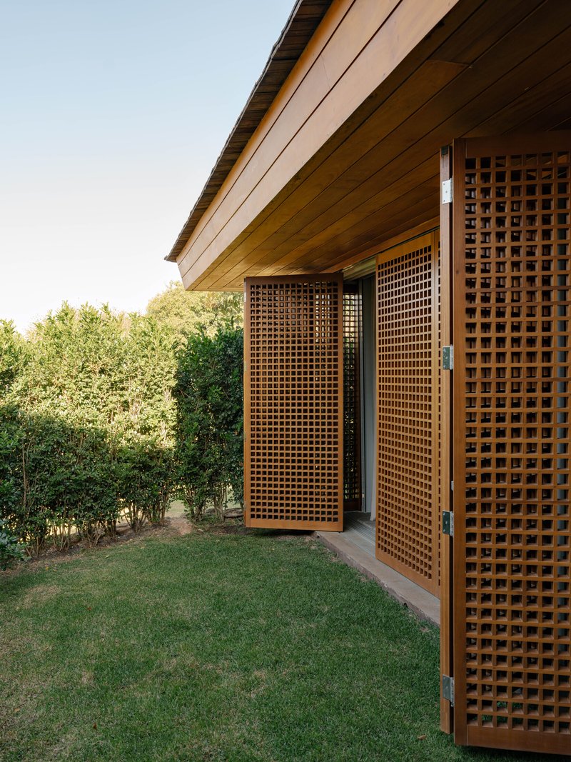 Exterior view of timber lattice screen doors opening onto lawn with timber soffit and dense hedge beyond