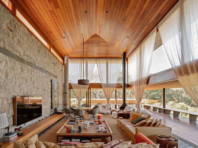 Double-height living room with stone fireplace wall and wood slat ceiling under sheer curtains
