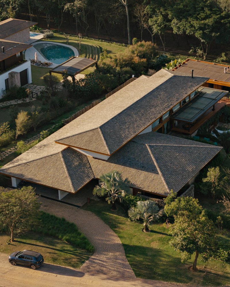 Aerial view of intersecting gable roofs with clay tiles and timber eaves among palm trees and lawn