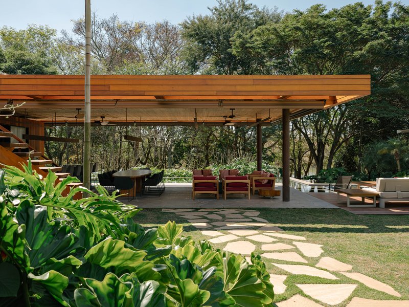 Covered outdoor terrace with exposed timber beams and stone paver pathways through planted beds