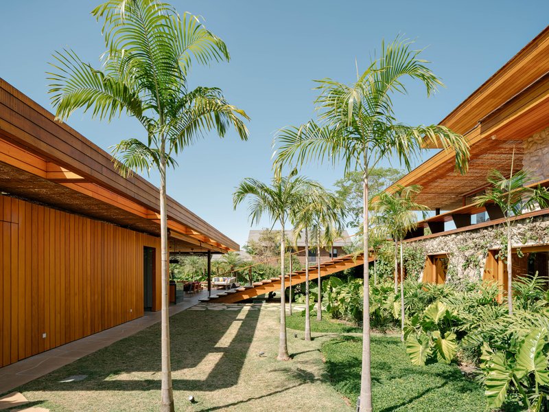 Courtyard with palm trees connecting the timber-clad volumes beneath sloped wooden roofs and exposed stone walls