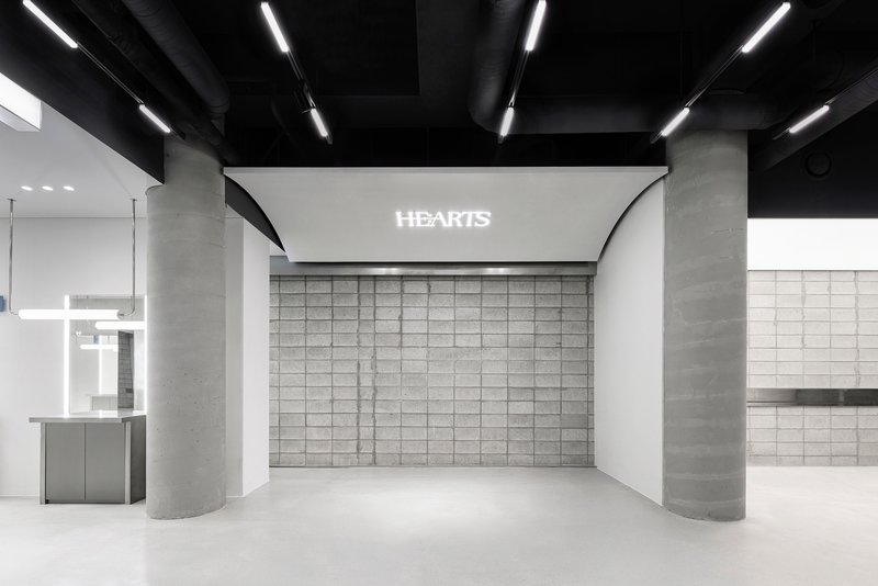 Gridded concrete block wall with illuminated signage flanked by cylindrical concrete columns