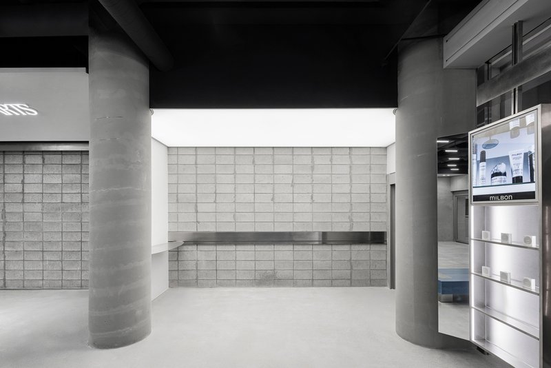 Display alcove with gridded block wall, floating shelf and cylindrical concrete columns under black ceiling