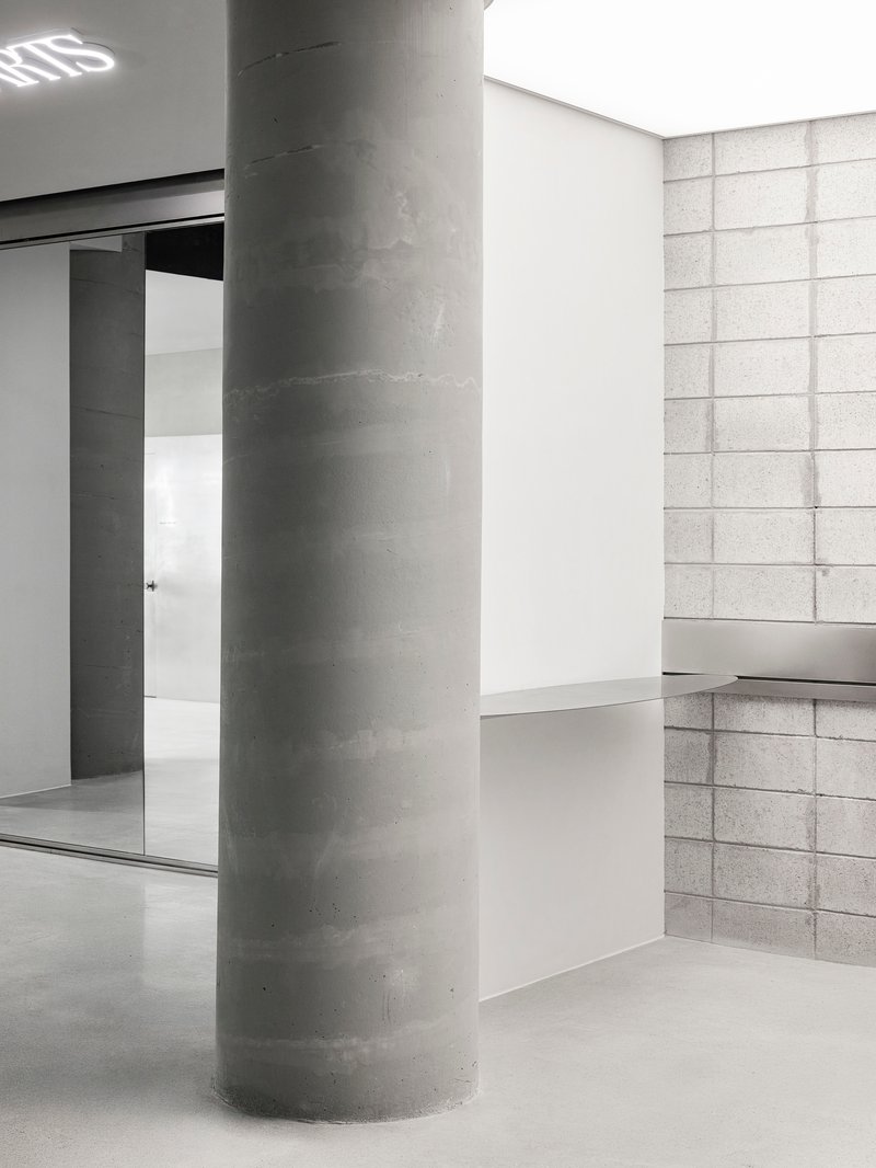 Concrete column in a white-walled interior with gridded stone block wall and polished floor