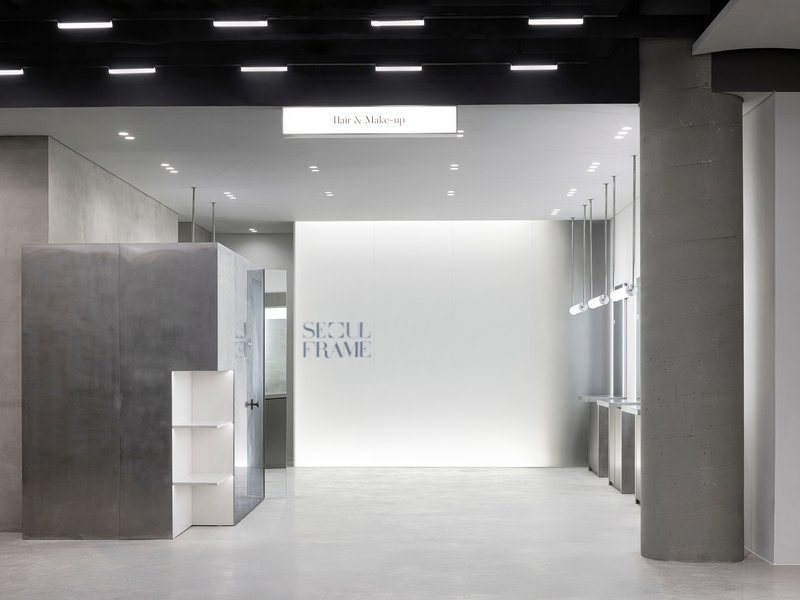 Retail interior with concrete columns and white wall displaying signage under linear ceiling lights