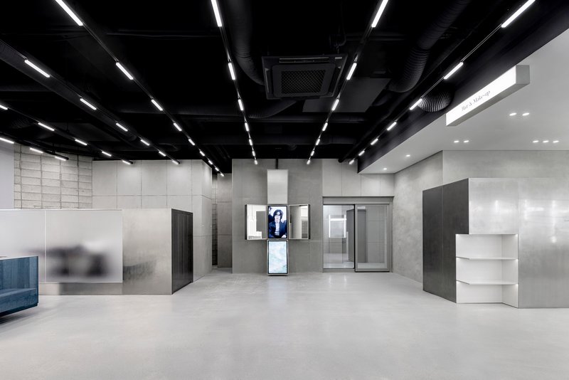 Open commercial space with exposed black ceiling ducts and linear lighting above display screens