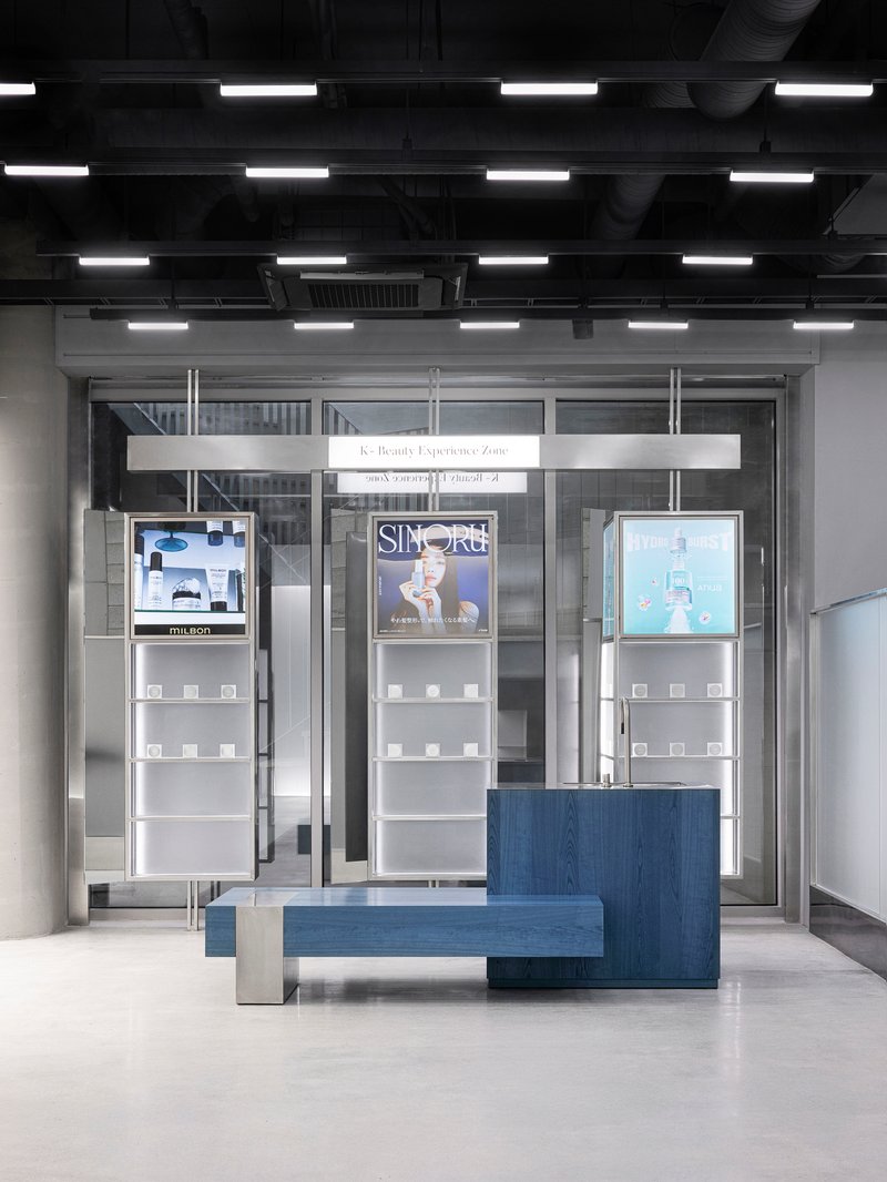 Glass entrance with product displays and blue bench under grid of linear ceiling fixtures