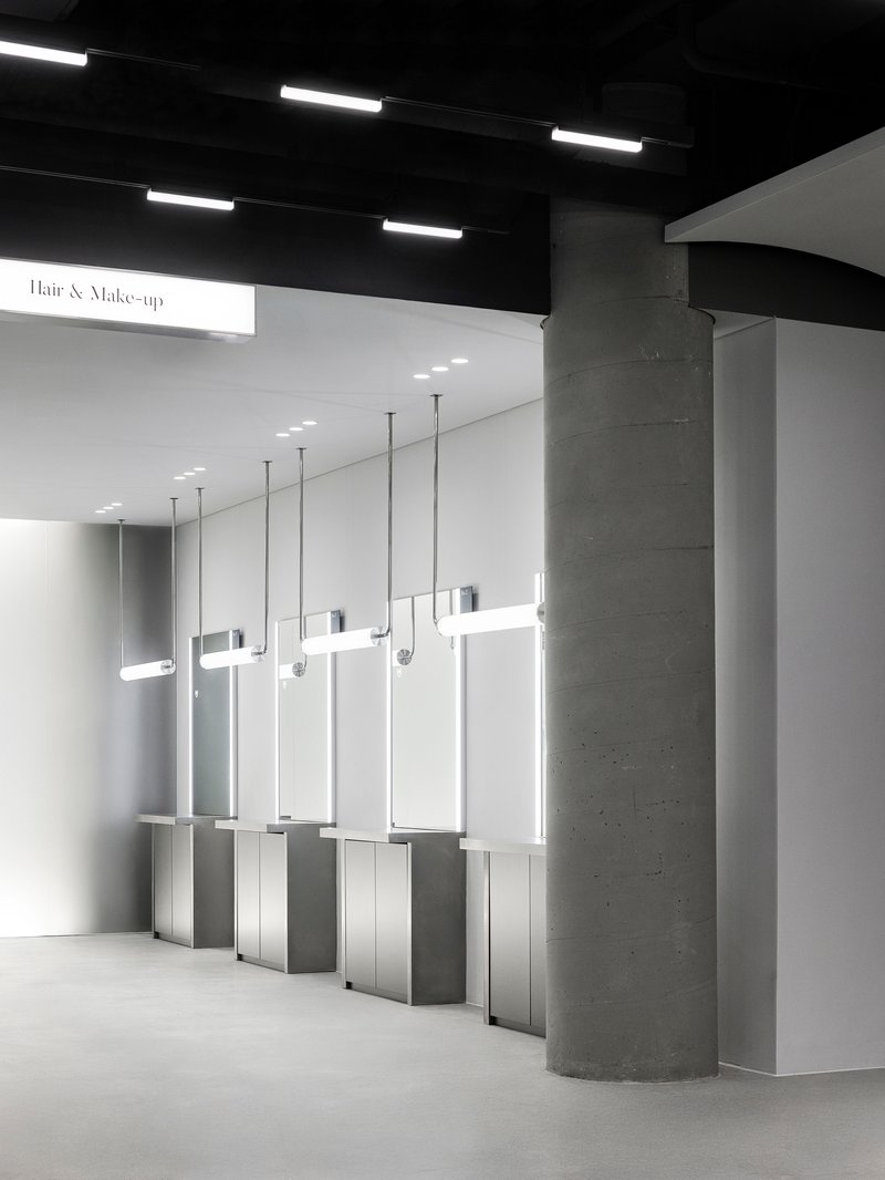 Row of backlit mirrors suspended from the ceiling with circular concrete columns against white walls