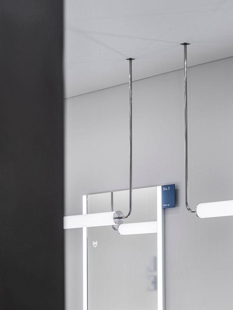 Detail of ceiling-mounted rod suspension system with numbered signage on translucent glass partition