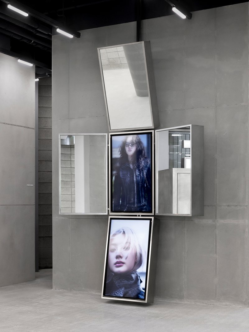 White display unit with pivoting screens showing portrait images against concrete panel walls