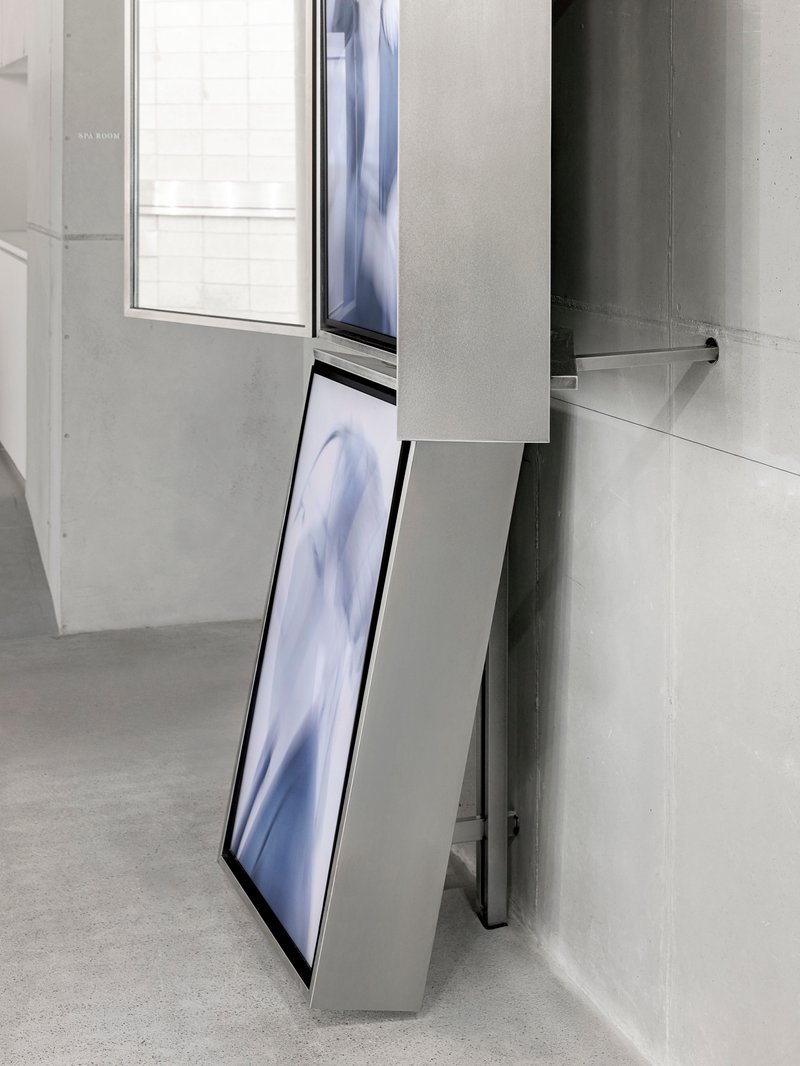 Tilted digital screen mounted to white volume beside window opening in concrete wall