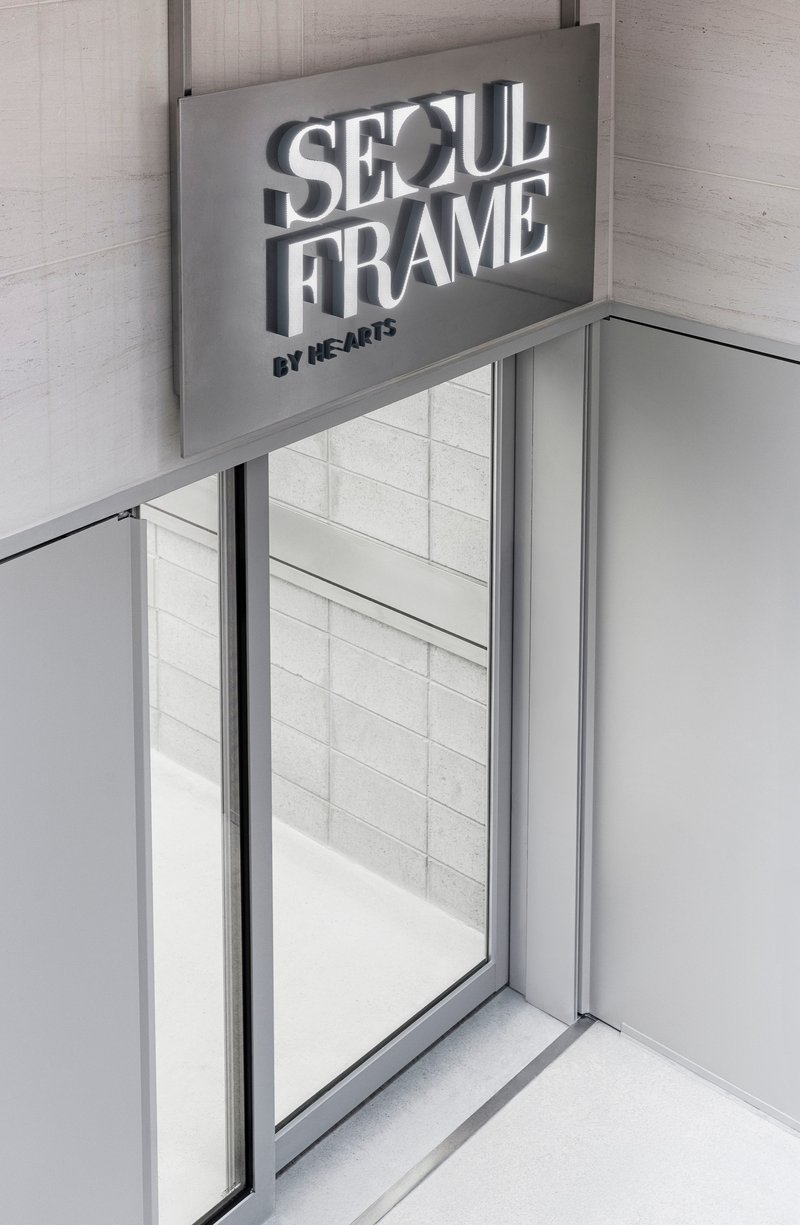 Glass entrance with aluminum frame beneath an overhead signage panel and pale tiled walls