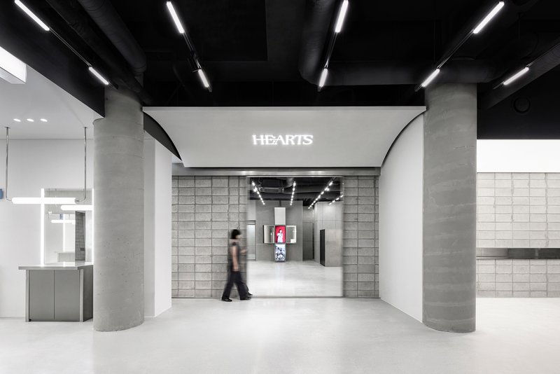 Interior hall with concrete columns and black exposed ceiling beams as a person walks through
