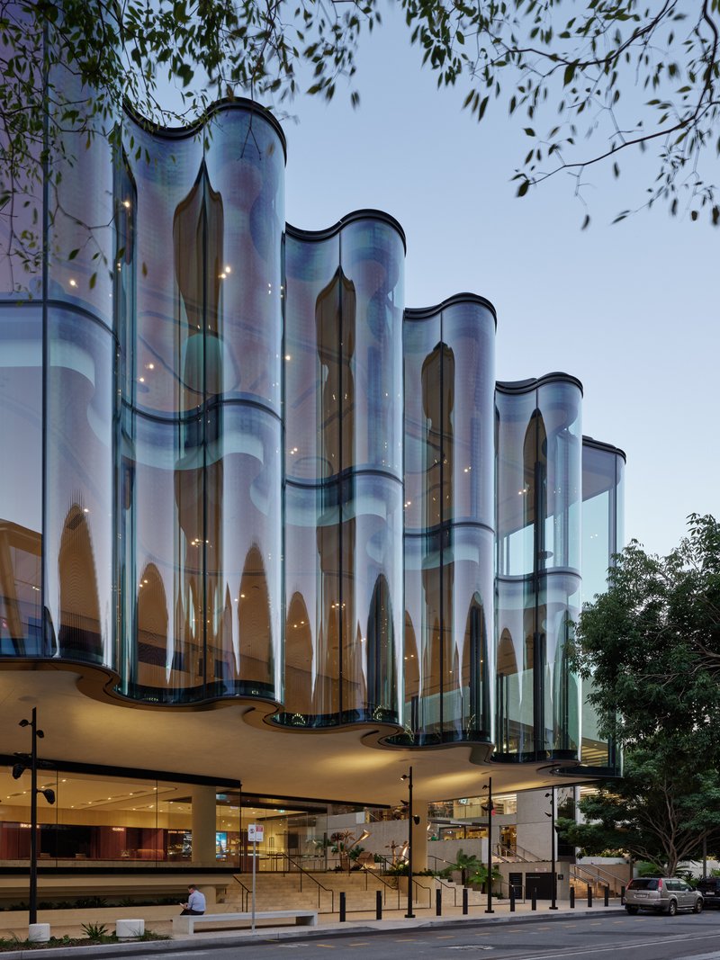 Side view of the cylindrical glass facade columns rising above the cantilevered podium at dusk