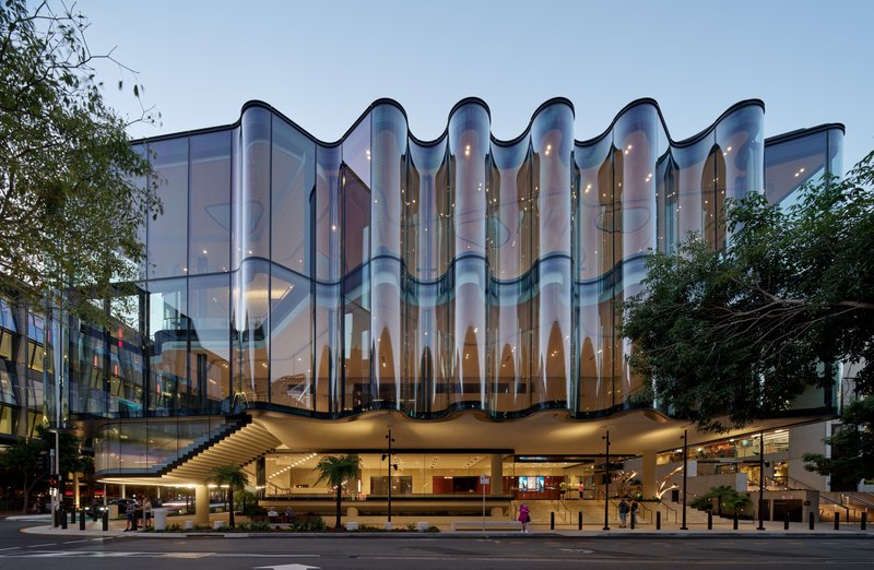 Frontal elevation showing the scalloped glass curtain wall above the open ground floor colonnade at twilight
