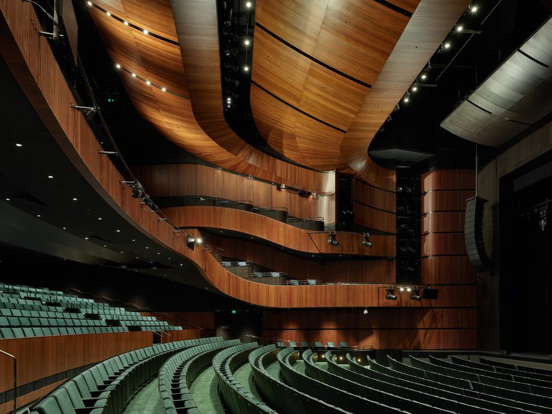 Interior view of the auditorium showing timber-clad curved balconies and rows of green upholstered seats