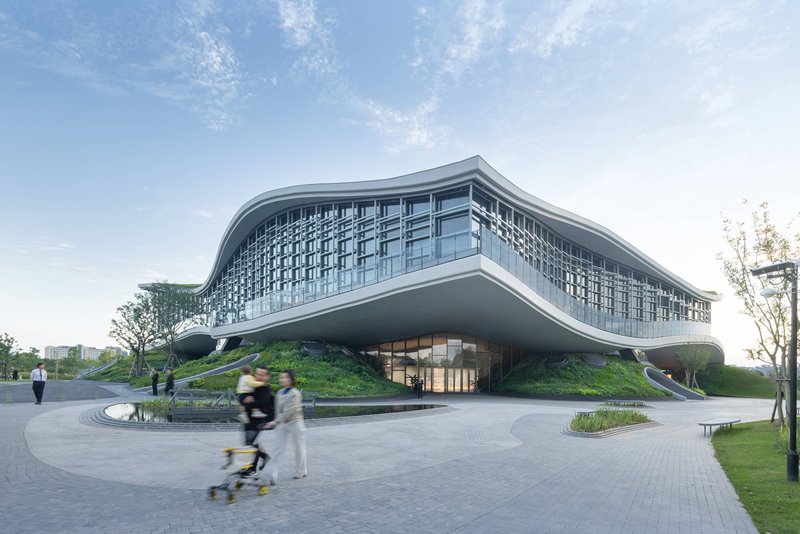 Entrance plaza with a curved water feature and pedestrians approaching the glass-walled facade on a clear day