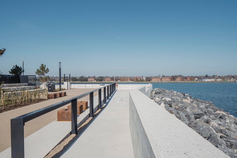 Waterfront promenade with timber benches between concrete walls and rocky shoreline