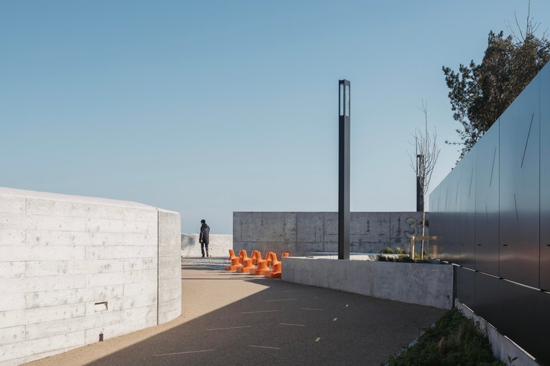 Plaza with concrete walls, tall black metal light post, and orange sculptural elements on a planter