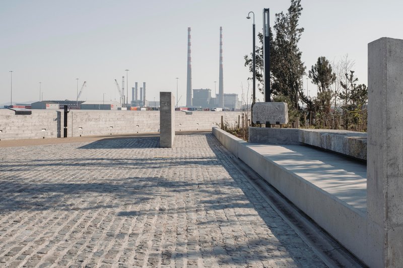 Granite block paving and concrete benches overlooking industrial harbor infrastructure in the distance