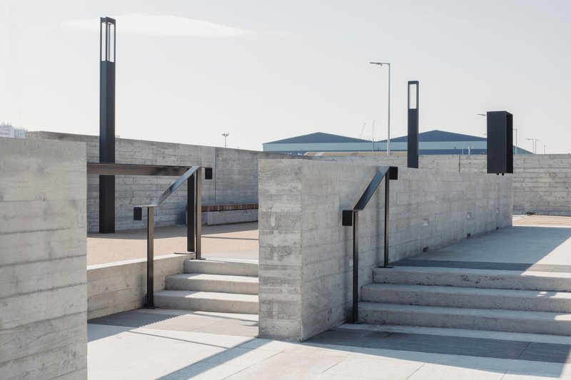Concrete staircases descending between perpendicular walls with black metal railings under overcast sky