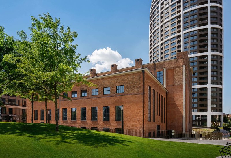 Red brick building with tall gridded windows beside a green lawn and leafy trees