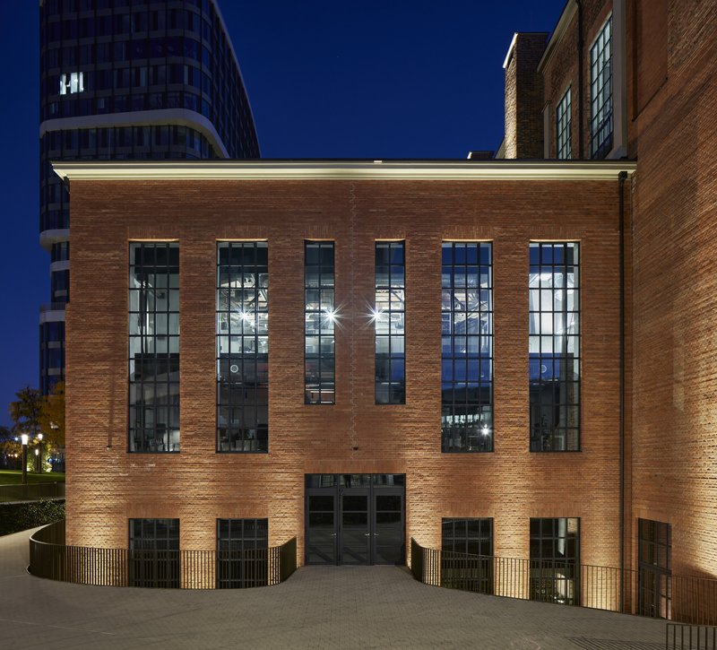 Curved brick facade with tall gridded windows and uplighting at night