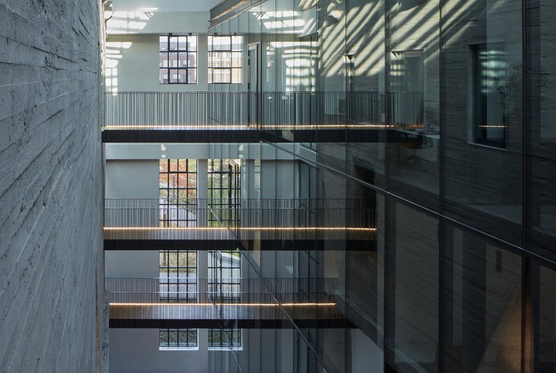 Interior atrium with stacked walkways and glass railings casting striped shadows across white walls