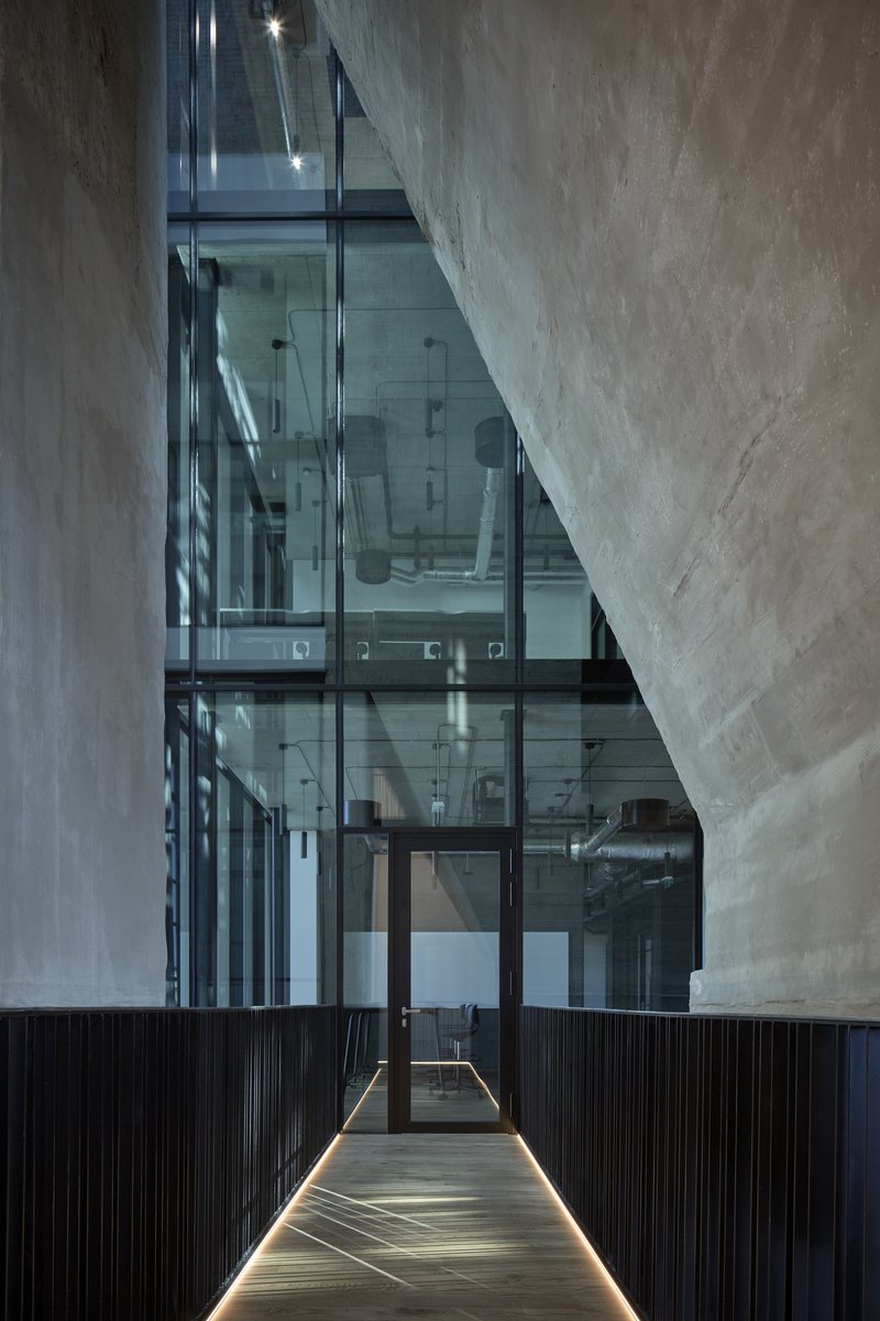 Narrow corridor with black metal wall panels and glass elevator shaft lit from below