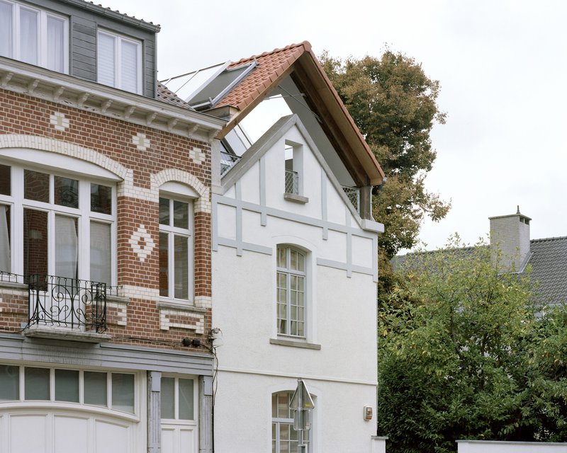 White rendered facade with half-timbered gable and terracotta tile roof beside a brick townhouse with trees