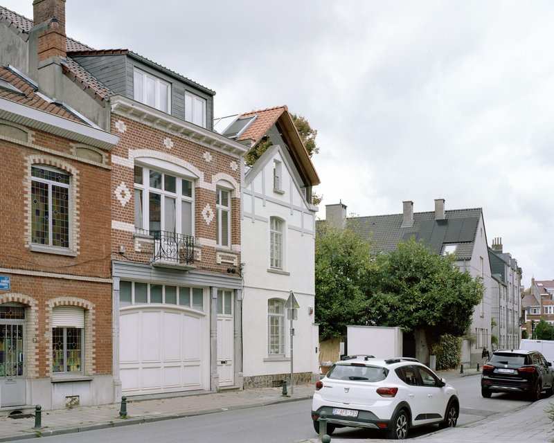 Street view showing white gabled extension between ornate brick buildings with parked cars in foreground
