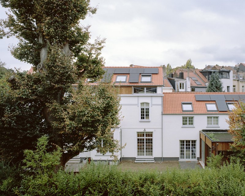Rear view of white rendered facades with terra cotta tiled roofs amid lush garden foliage