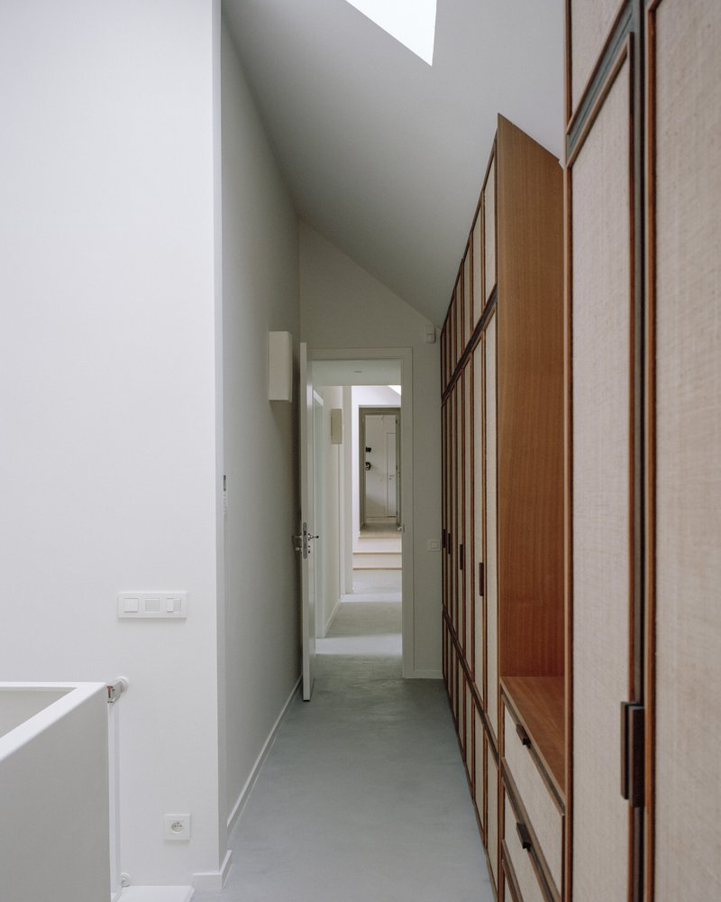 Narrow hallway with timber-framed storage units and grey resin flooring beneath a skylight
