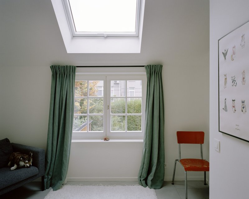 Bedroom with skylight above a white casement window framed by green curtains