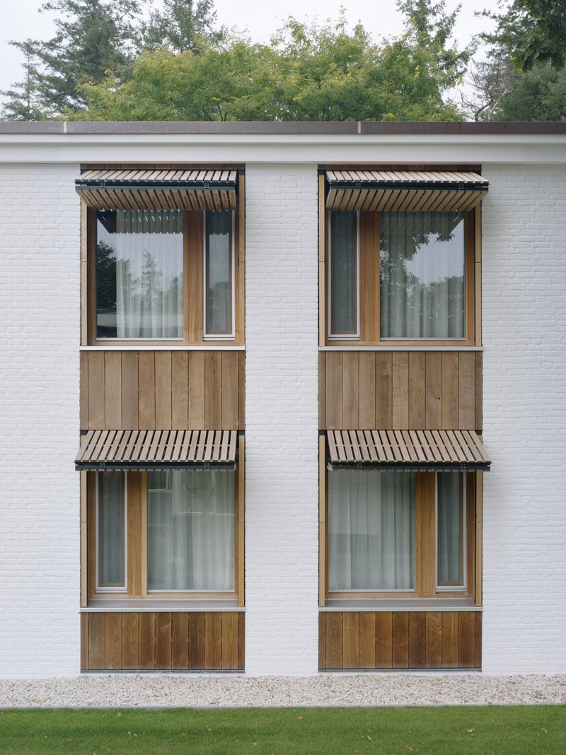 Four stacked windows with timber cladding and corrugated metal awnings on a white brick wall