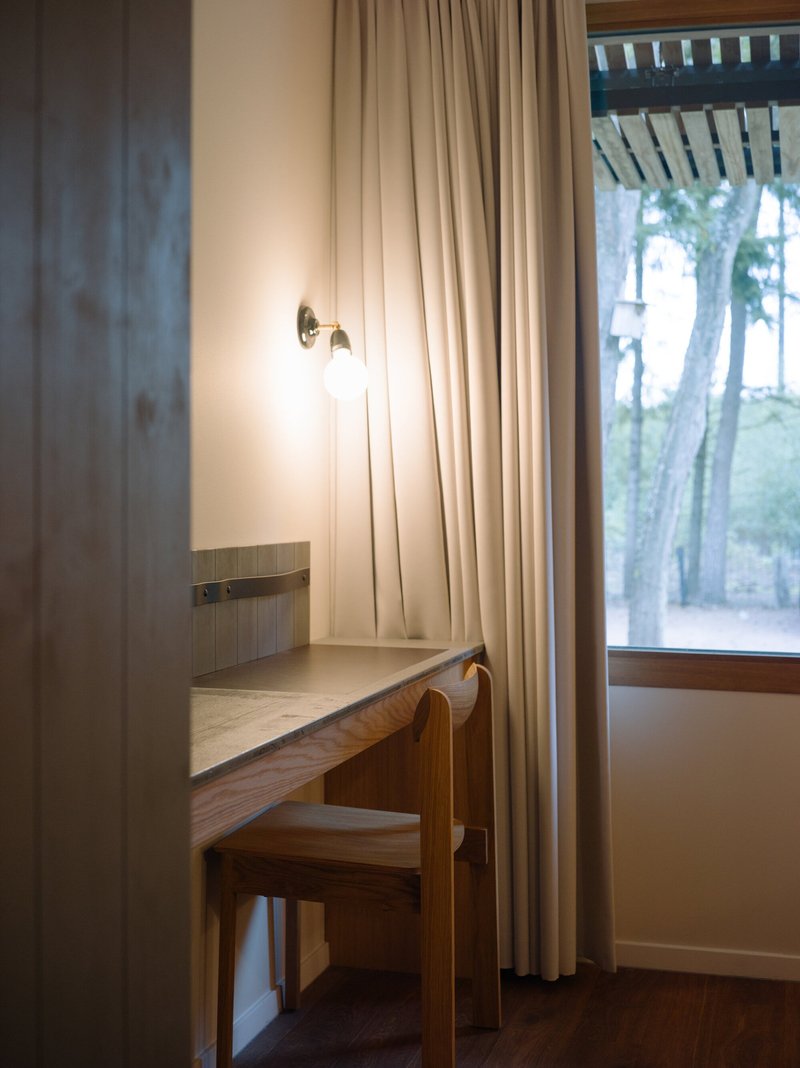 Built-in desk with wall sconce and beige curtains beside a window overlooking trees at dusk