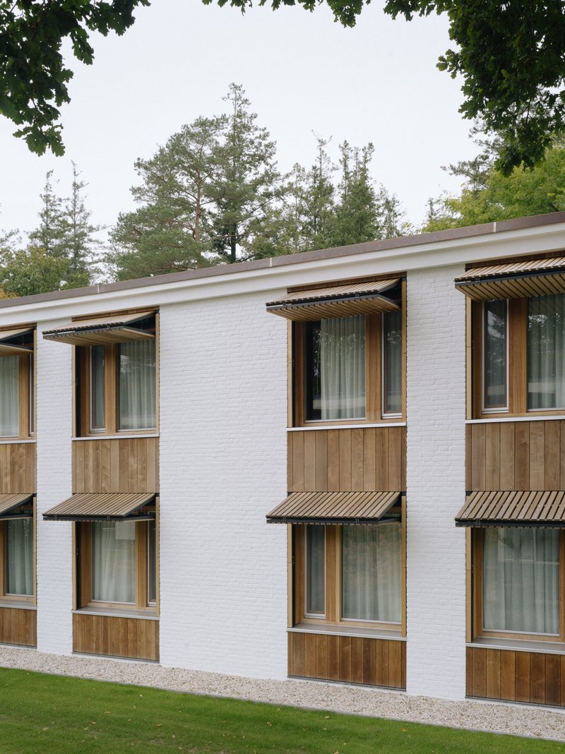 Repeating facade rhythm of timber balconies with slatted awnings and gravel beds framed by trees